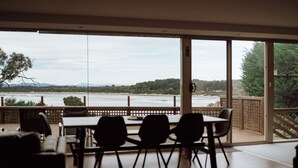 A dining area with a table and chairs, large windows with a view of a river and hills. - Beachfront Retreat with Direct Beach Access | Family Friendly (Greens Beach)