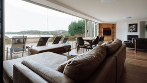 A modern living room with a large window overlooking a scenic view, a dining area, and a fireplace. - Beachfront Retreat with Direct Beach Access | Family Friendly (Greens Beach)