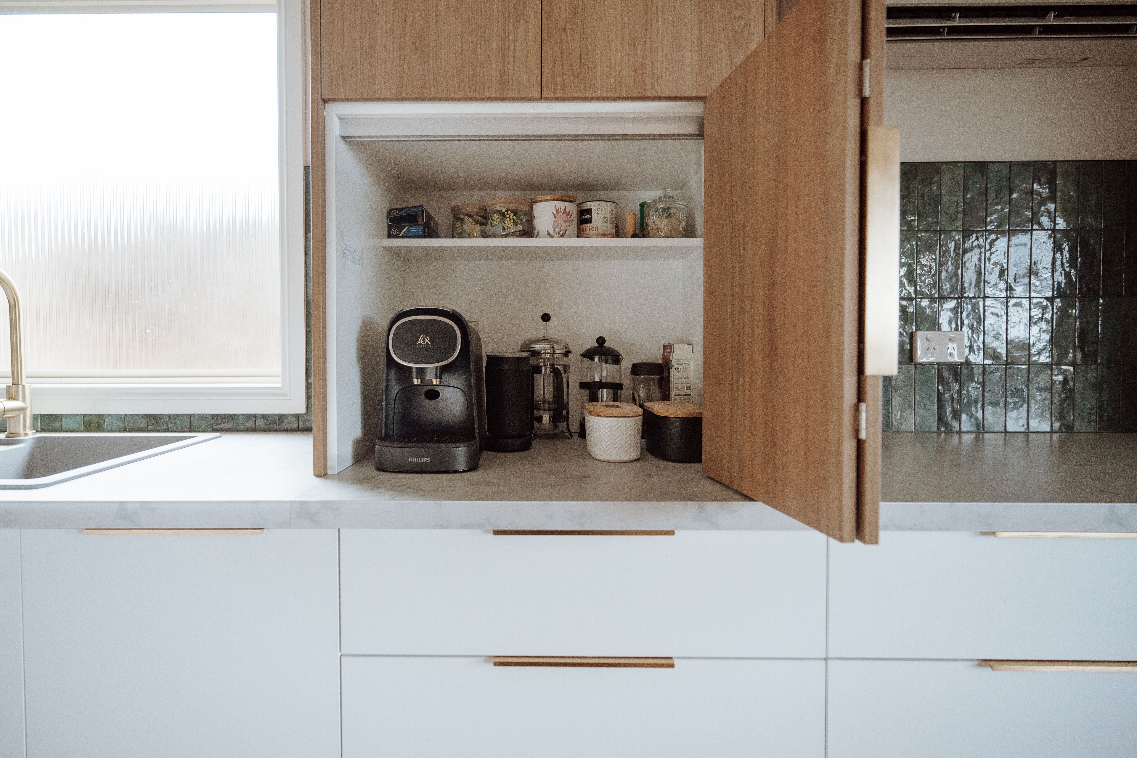 A kitchen with white cabinets, a coffee maker, and various containers on the shelves.