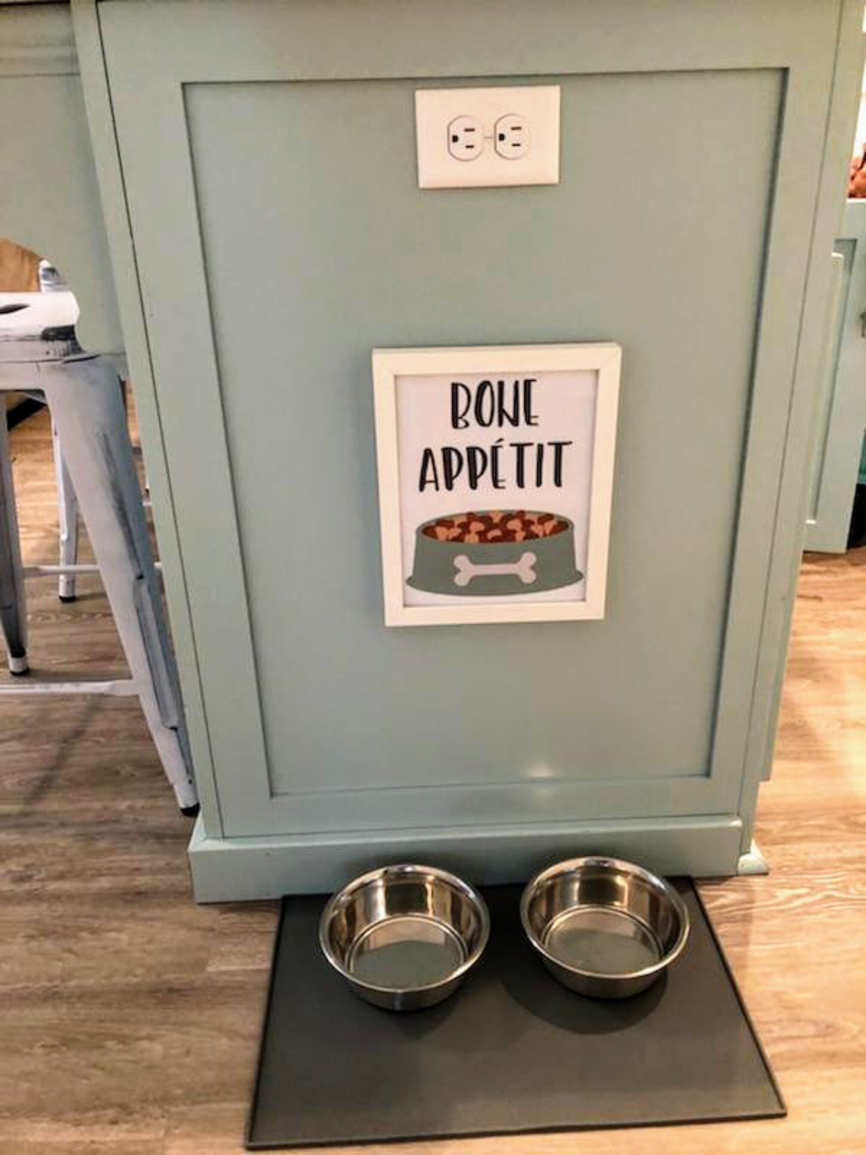 Eine Küchenzeile mit einem gerahmten Schild mit der Aufschrift 'BONE APPETIT' und zwei Metallschüsseln auf einer Matte.