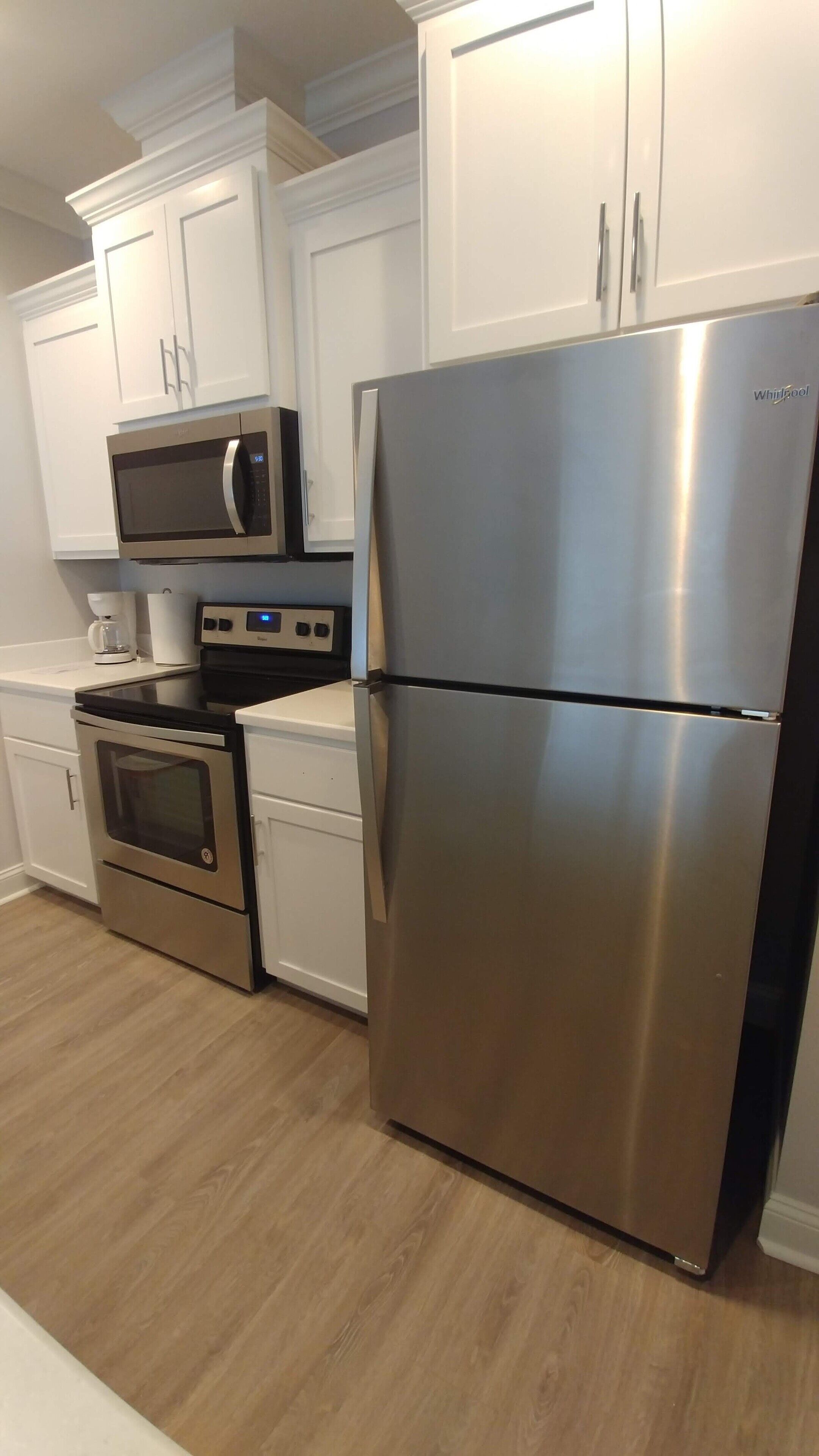 A kitchen with white cabinets, a stainless steel refrigerator, a microwave, and an oven.