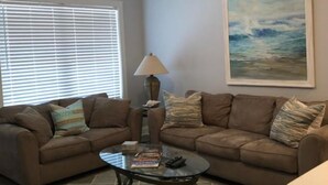 A living room with two brown sofas, a glass coffee table, a lamp, and a painting on the wall.