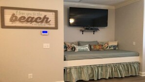 A bedroom with a bed, a television mounted above it, and a wall with a decorative sign.