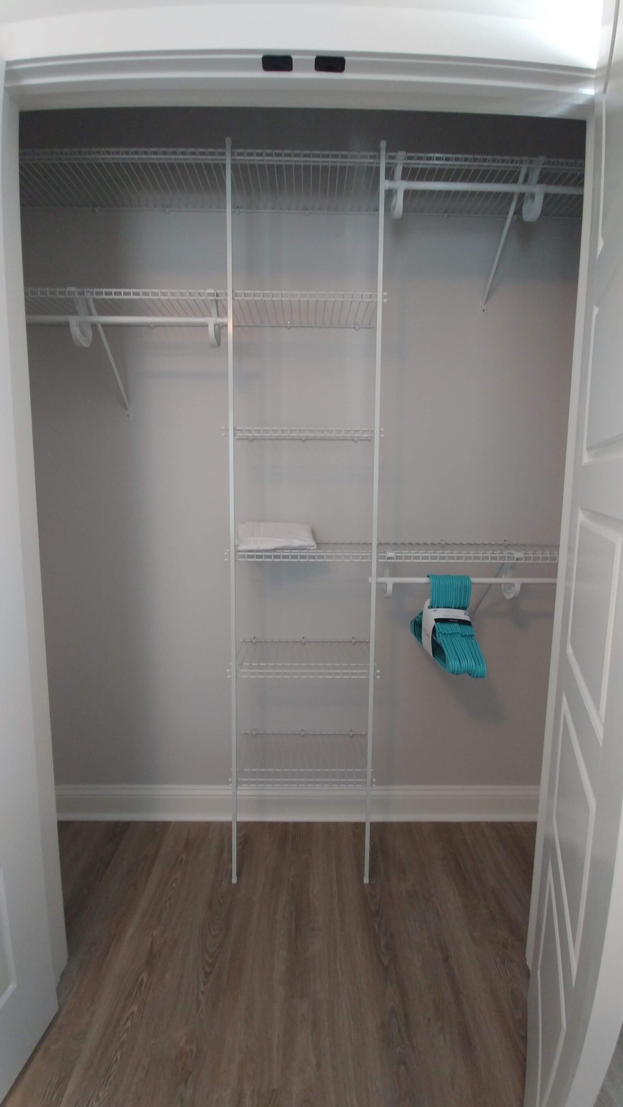 A walk-in closet with multiple shelves and hanging space, wooden flooring, and a white door.