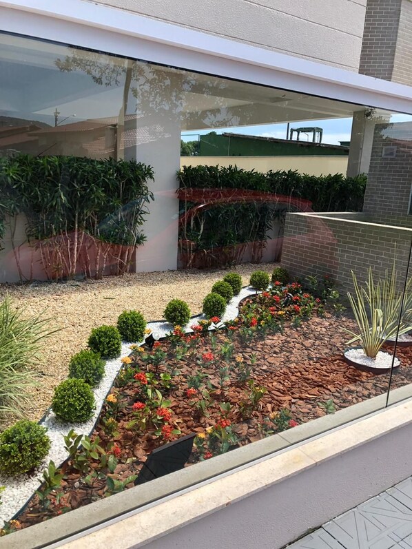 A modern outdoor garden with neatly arranged shrubs and a variety of plants, including a section with red flowers and a small water feature.