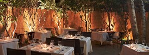 Un área de comedor al aire libre con mesas dispuestas para una comida, rodeada de paredes de bambú y árboles.