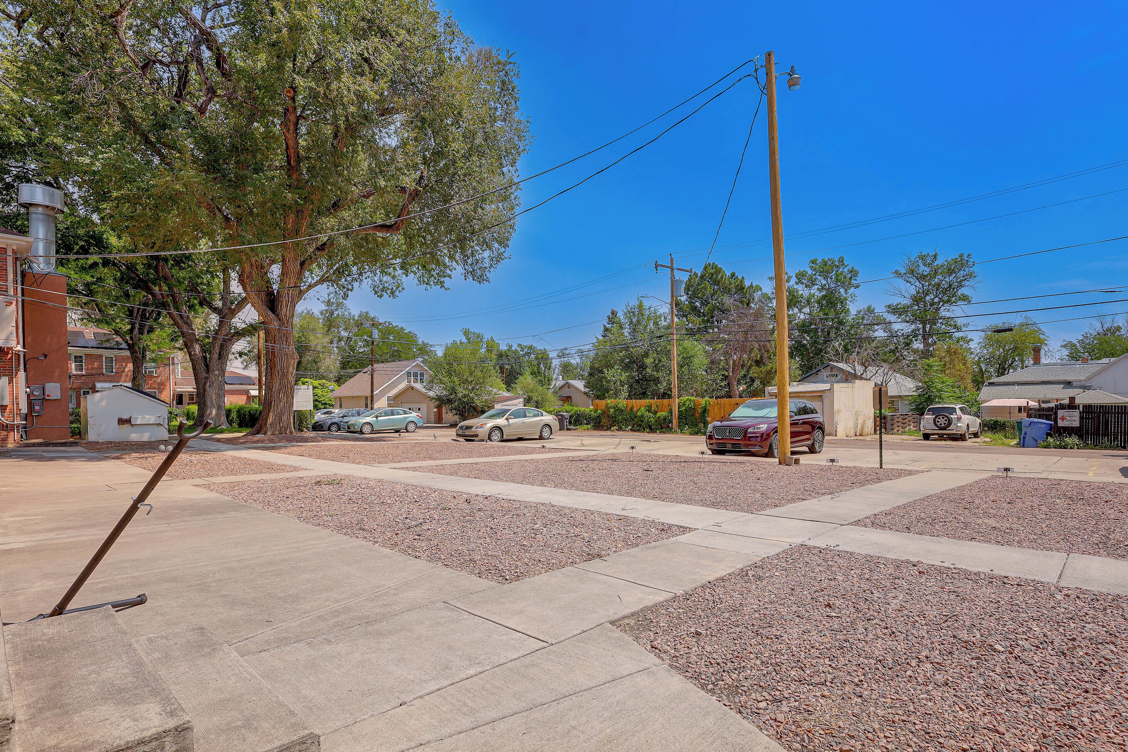 A residential street with parked cars, houses, and a clear blue sky.