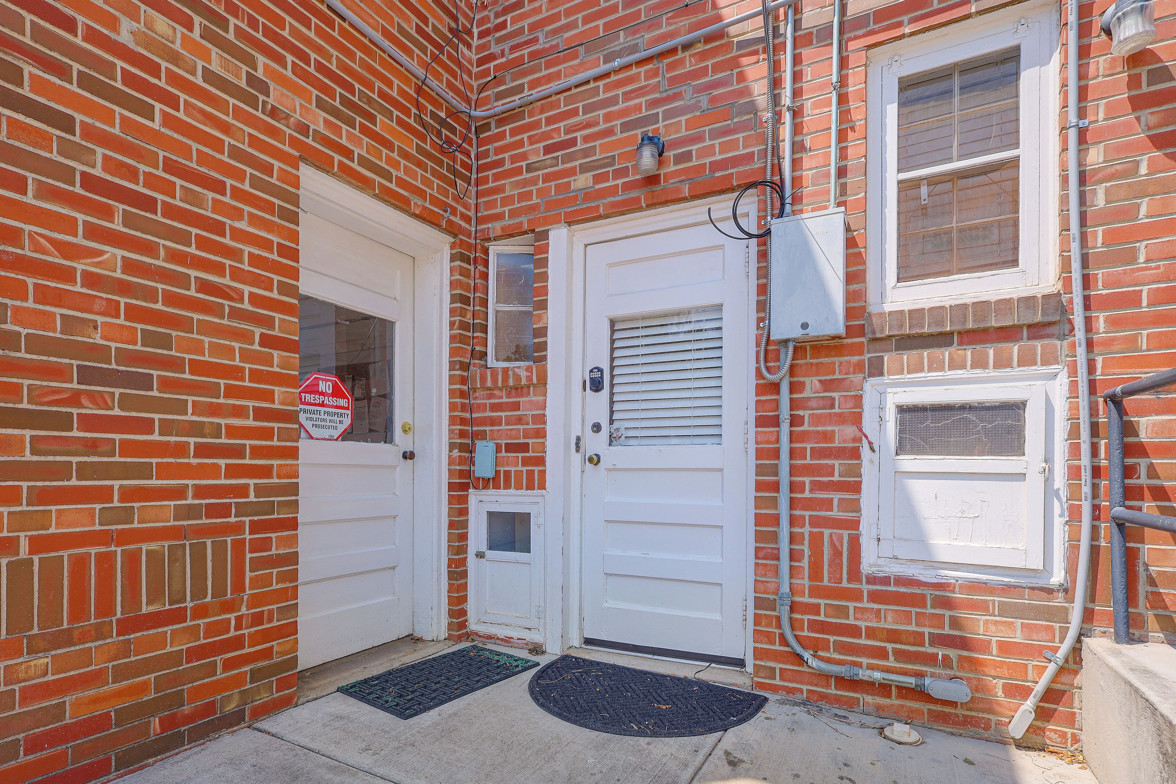 A red brick building with two white doors, a window with blinds, and a no trespassing sign.
