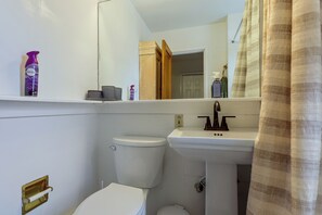 Un baño con inodoro, lavamanos y espejo sobre él. Hay artículos de aseo en la encimera.