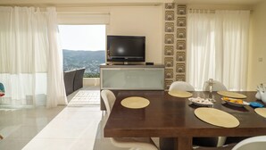 Un coin repas avec un téléviseur posé sur un meuble, une table dressée avec des sets de table, des assiettes et une bougie.