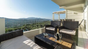 Un balcon doté de meubles en osier, d’une table en verre et offrant une vue sur les montagnes.
