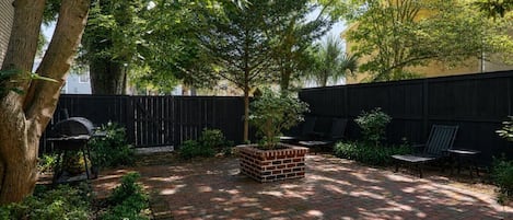 A backyard with a brick patio, a grill, a brick planter, and outdoor furniture.