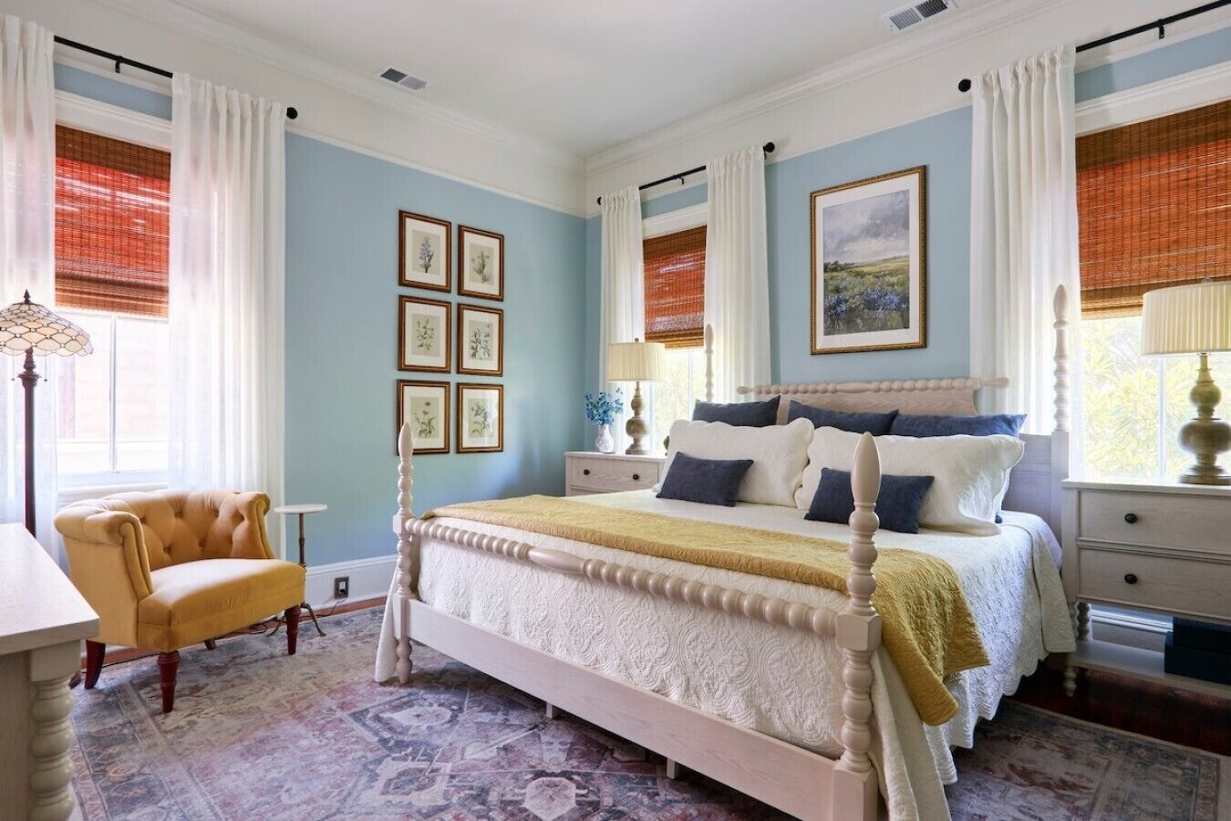 Quarto com cama de dossel, uma cadeira, mesa de cabeceira e janela com cortinas.