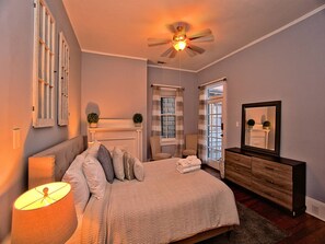 A bedroom with a bed, a dresser, a mirror, a ceiling fan, and a window with curtains.