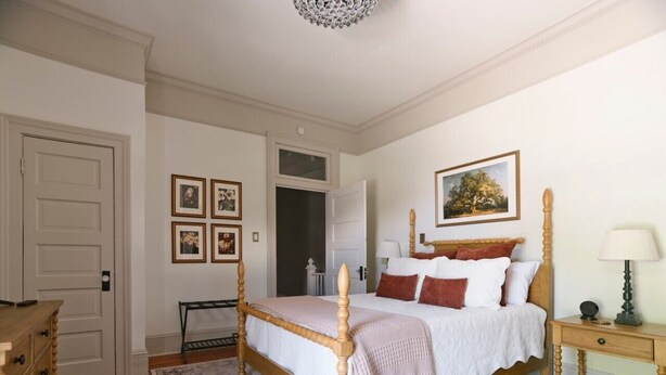 A bedroom with a four-poster bed, a bedside table, a dresser, and a framed picture on the wall. - Downtown Savannah Oasis 6 beds 3 baths (Savannah)