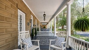 A covered porch with two rocking chairs and a small table, a brick wall, and a view of the street. - Downtown Savannah Oasis 6 beds 3 baths (Savannah)