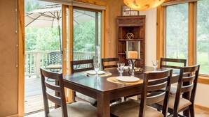 Een eetruimte met een houten tafel gedekt voor vier personen, omringd door stoelen. Er is een groot raam met uitzicht op groen.