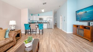 A spacious living room with a wooden floor, a sofa, a coffee table, and a dining area with chairs.