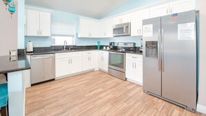A modern kitchen with white cabinets, stainless steel appliances, and a wooden floor.