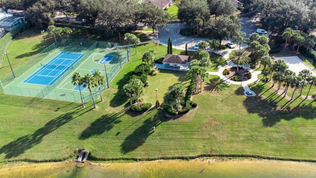 An aerial view of a residential area with a tennis court, a house, and a landscaped garden with palm trees.