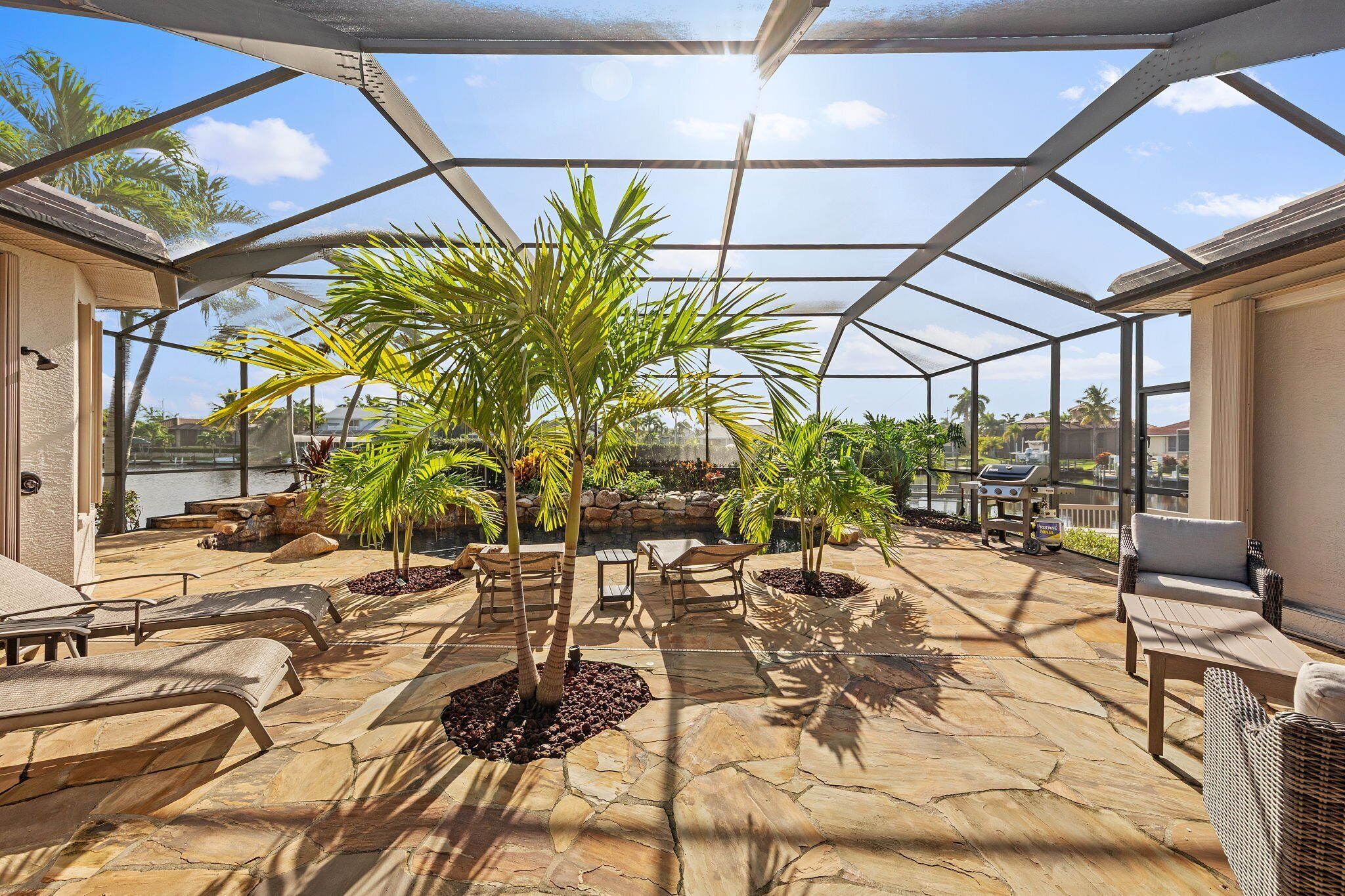 Een overdekt terras buiten met stenen vloer, lounge stoelen en potplanten.