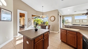 A kitchen with wooden cabinets, a granite countertop, and a dining area with a glass table and chairs. - Villa Portofino: Resort Style Pool, Gulf Access (Cape Coral)