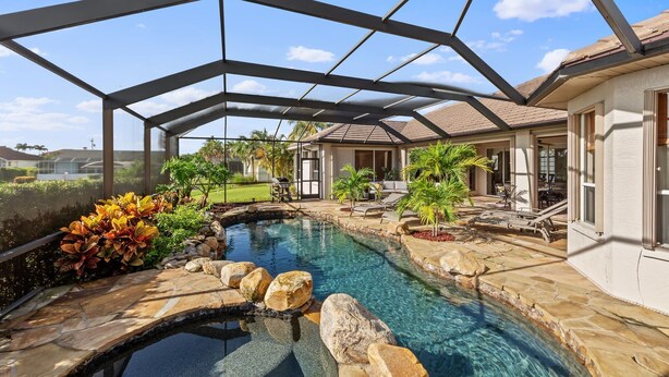 A swimming pool with a stone border and rocks, surrounded by a covered patio area with outdoor furniture. - Villa Portofino: Resort Style Pool, Gulf Access (Cape Coral)