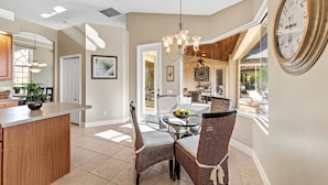 A dining area with a glass table, wicker chairs, and a chandelier. - Villa Portofino: Resort Style Pool, Gulf Access (Cape Coral)