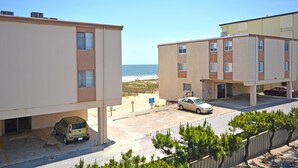 A coastal apartment building with a parking area, a beach view, and a small parking garage. - Cute, casual 2-bedroom condo with free WiFi and a partial ocean view located midtown and less than a block to the beach! (Ocean City)