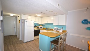 A compact kitchen with white cabinets, a wooden island, and a microwave. - Cute, casual 2-bedroom condo with free WiFi and a partial ocean view located midtown and less than a block to the beach! (Ocean City)