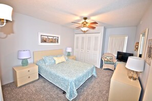 A bedroom with a bed, nightstands, a dresser, a television, a ceiling fan, and a door with a window.