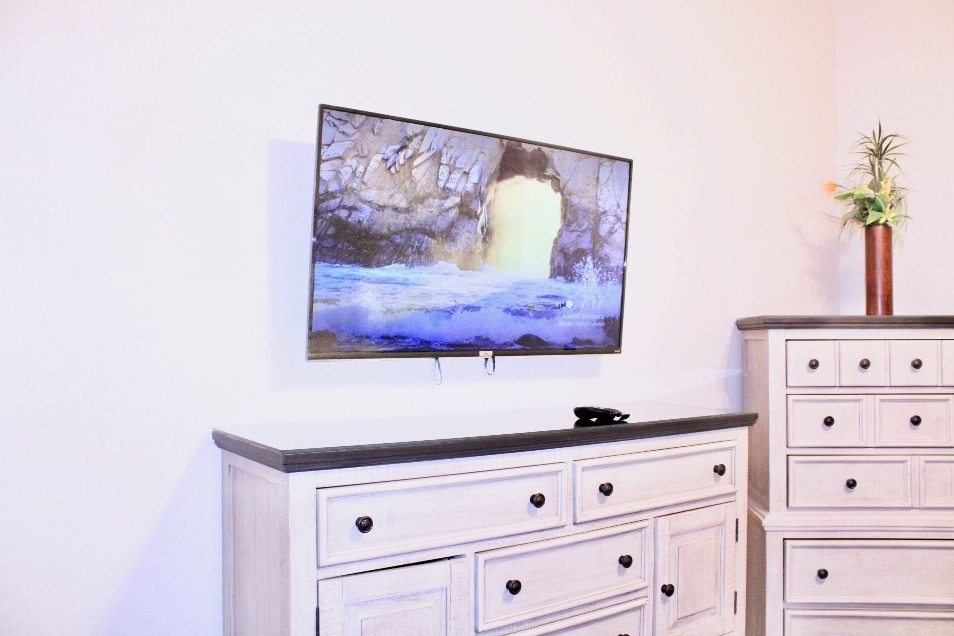 A television mounted on a wall above a white dresser with multiple drawers.