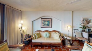 A cozy living room with a sofa, a coffee table, and a dining area. There is a framed picture on the wall and a vase with plants on the side table. - Bienvenido Amigo! In the heart of Amapas  2BD Condo for rent in Old Town, Puerto (Puerto Vallarta)