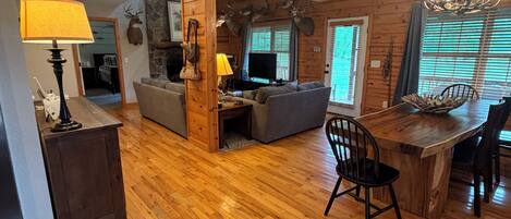 A living room with a fireplace, wooden flooring, a dining area with a wooden table and chairs, and a television.