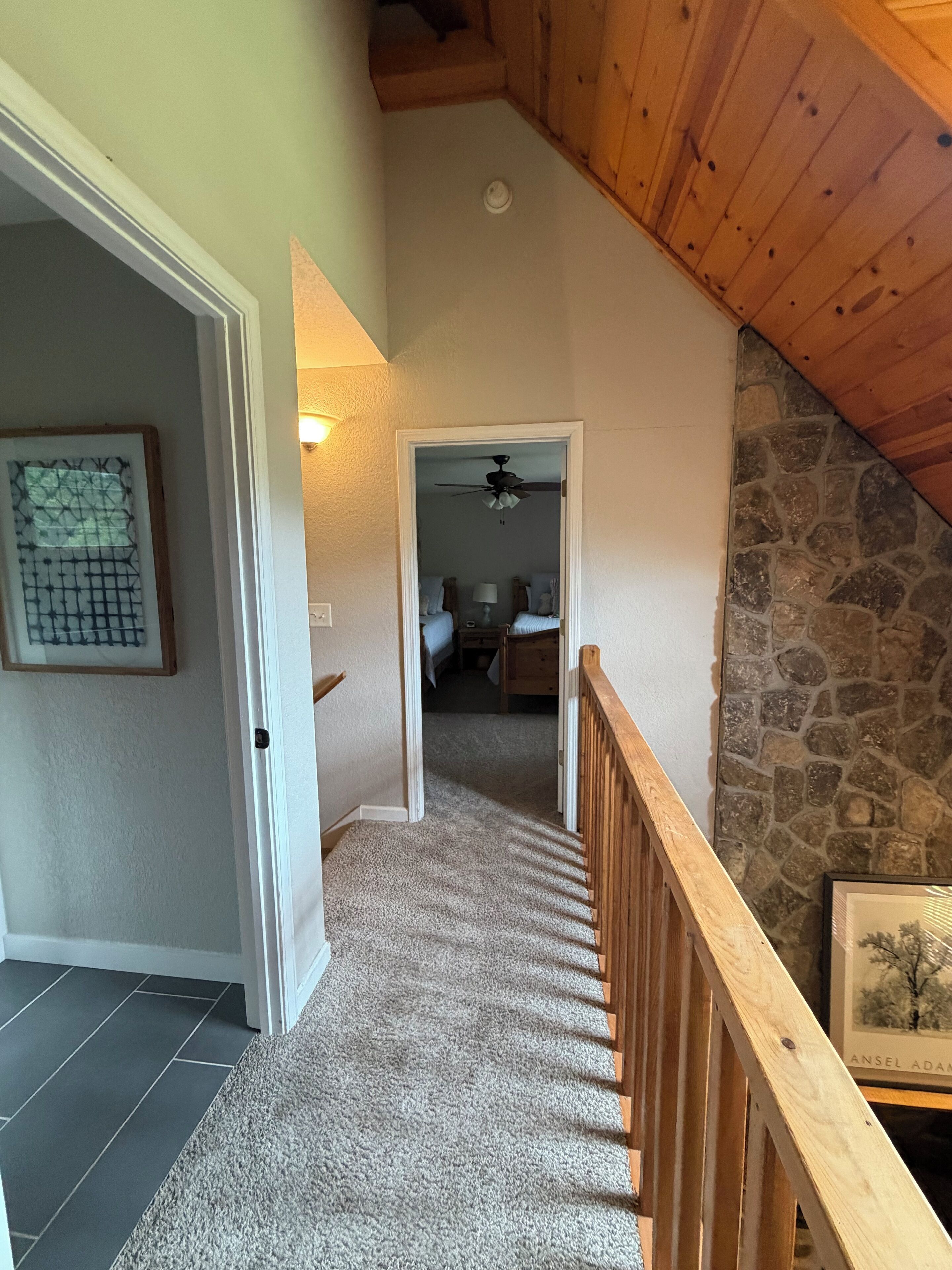 A staircase with a wooden railing leading to a bedroom with a stone wall and a ceiling fan.