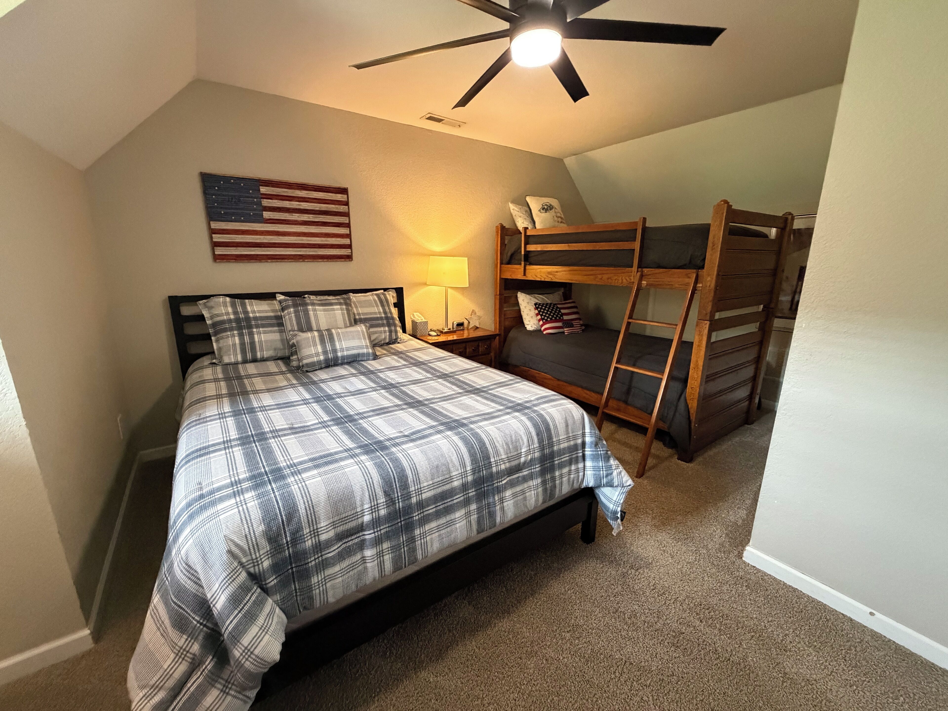 A bedroom with a bed, a ceiling fan, a bunk bed, and an American flag on the wall.