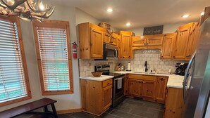 Una cocina con armarios de madera, un refrigerador de acero inoxidable, un horno empotrado y un banco.