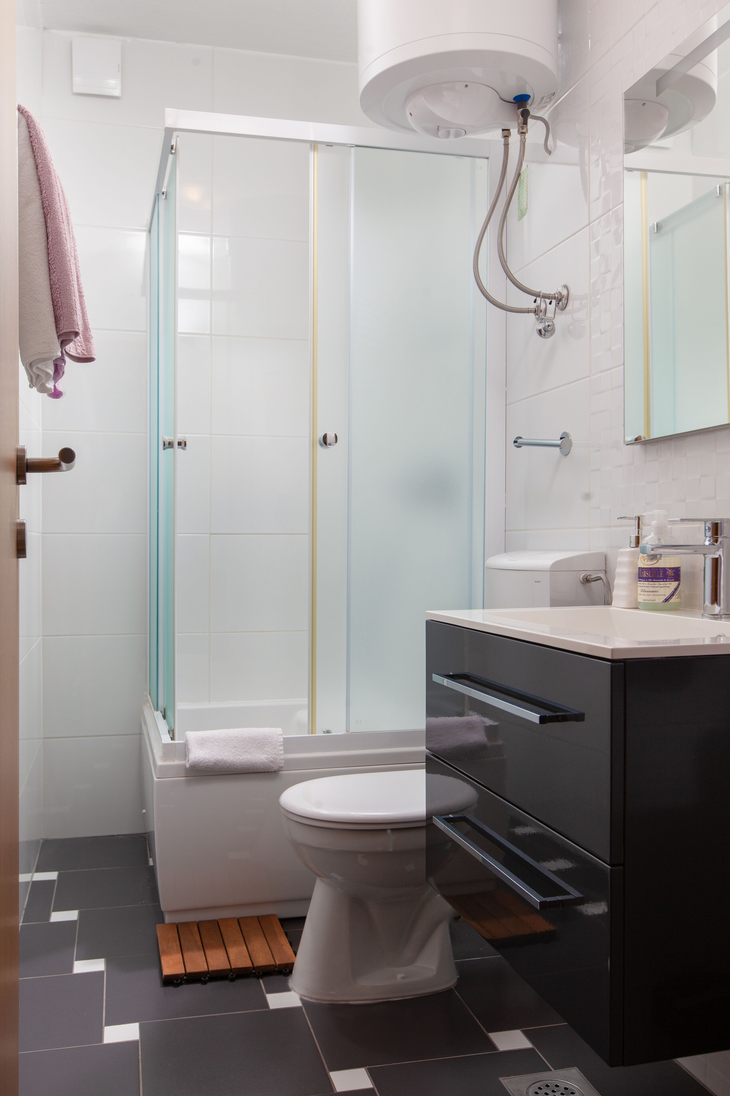 Een moderne badkamer met een douchecabine van glas, een wit toilet, een zwart kastje en een spiegel boven de wastafel.