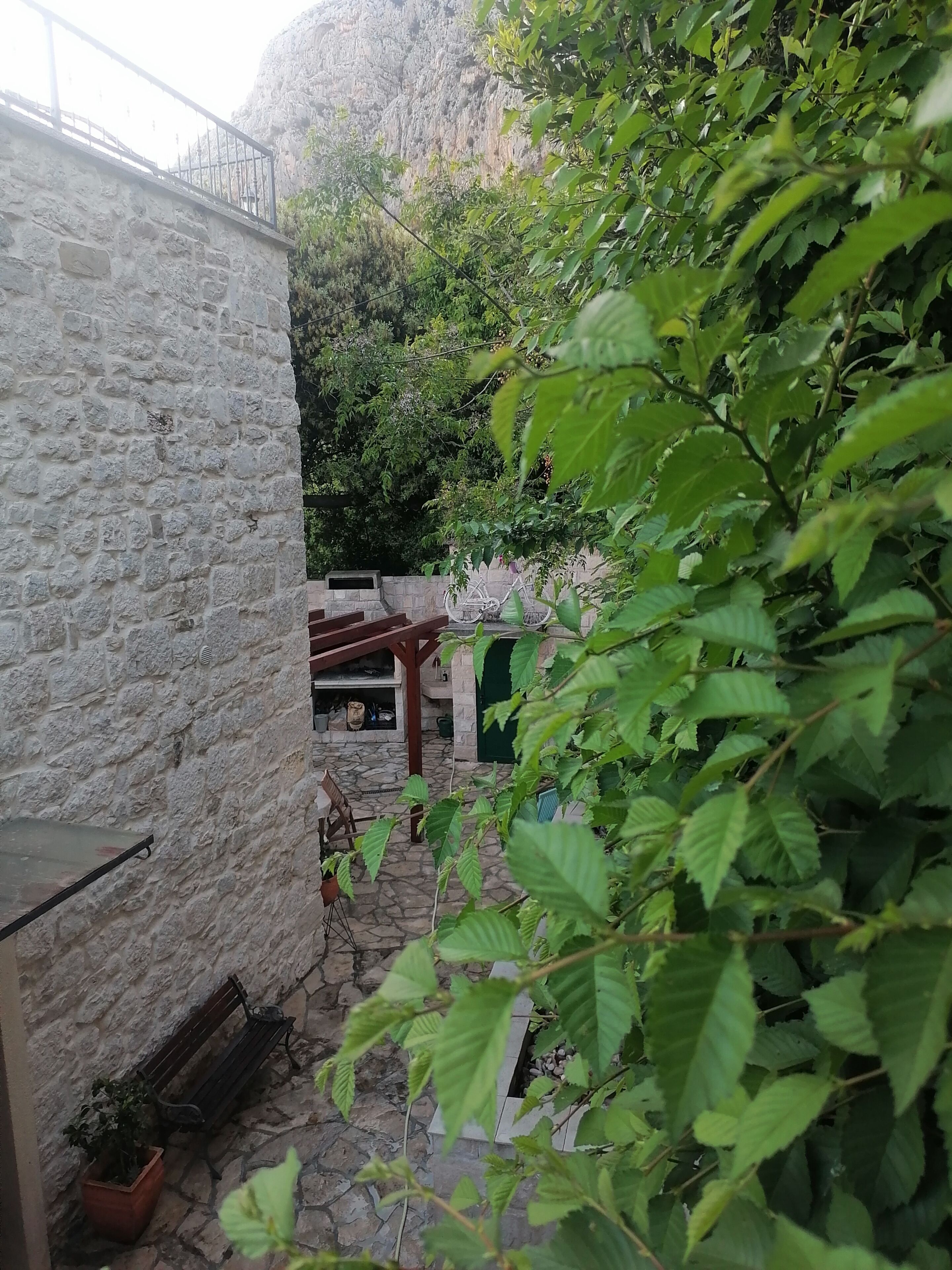 Un mur de pedra, una cadira de fusta i una barana de metall en una zona de jardí.