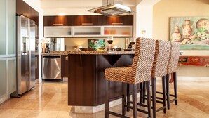 A modern kitchen with a central island, stainless steel appliances, and dark wooden cabinetry.