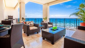 A balcony with wicker furniture, a dining table, and a view of the sea.