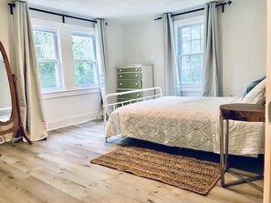 Una camera da letto con un letto, una cassettiera e due finestre.