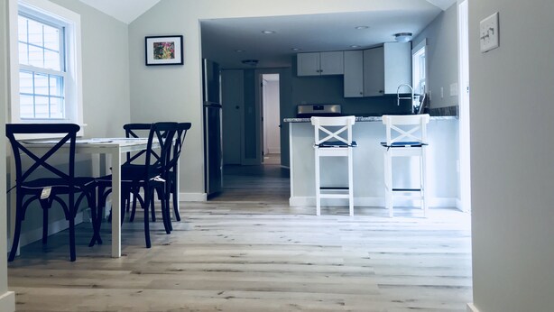 A modern kitchen with white cabinets, a central island, and a dining area with a table and chairs.
