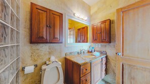 Un baño con armarios de madera, encimera de mármol, lavabo e inodoro.
