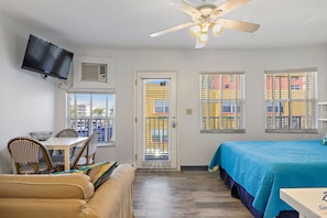 A hotel room with a bed, a dining table with chairs, a television, and a ceiling fan.