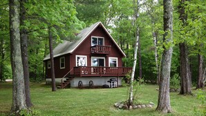 A cabin with a porch, a deck, and a grill area. - Waterfront Chalet with private beach in the White Mountains of New Hampshire. (Conway)