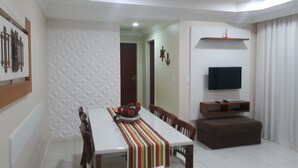 A dining area with a table and chairs, a television on a stand, and a decorative wall. - Fully furnished apartment with 2 parking spaces. (ARRAIAL DO CABO)