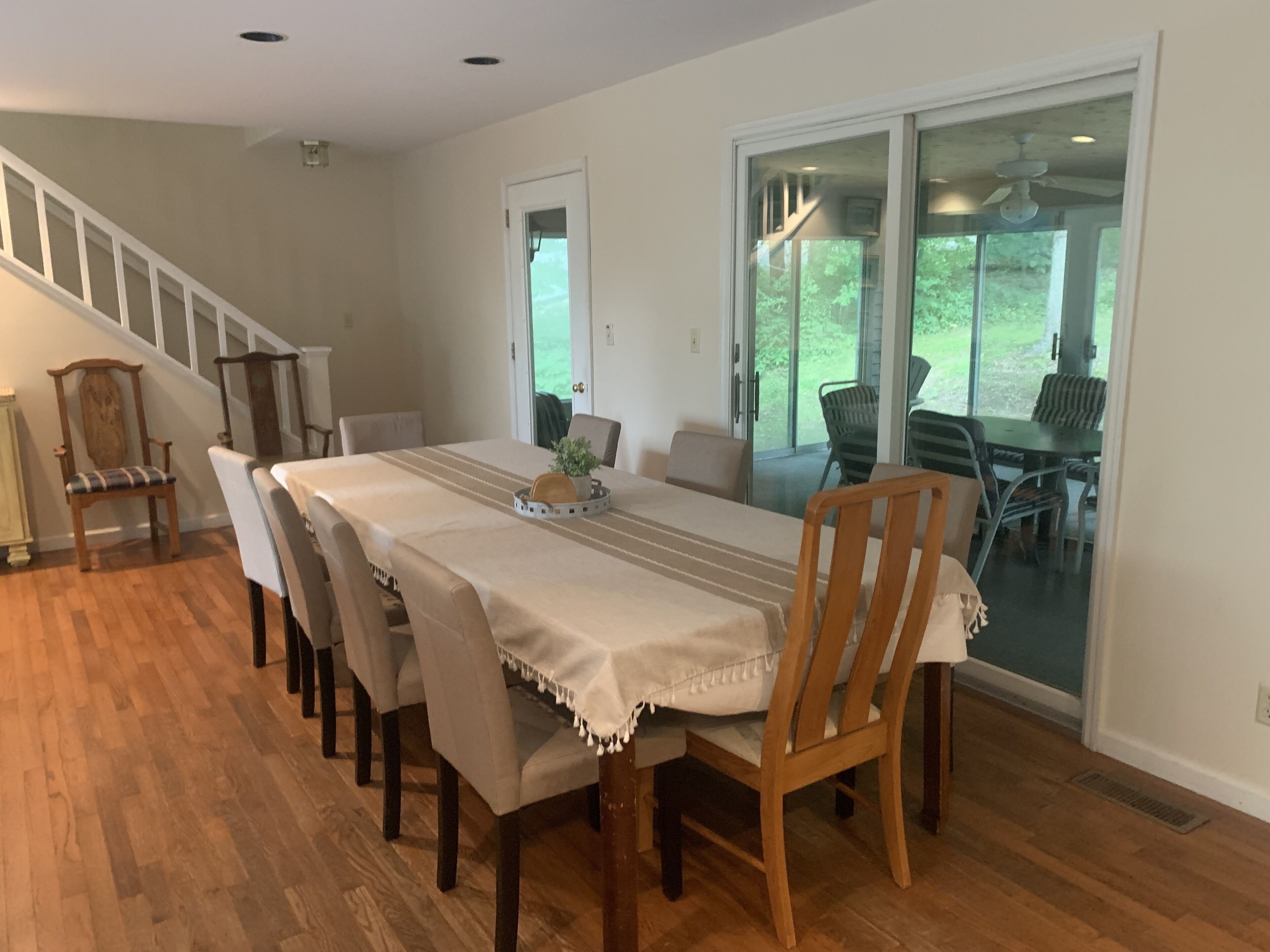 A dining area with a long table, chairs, and a staircase leading to a balcony.