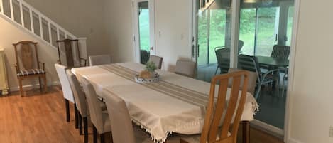 A dining area with a long table, chairs, and a staircase leading to a balcony.