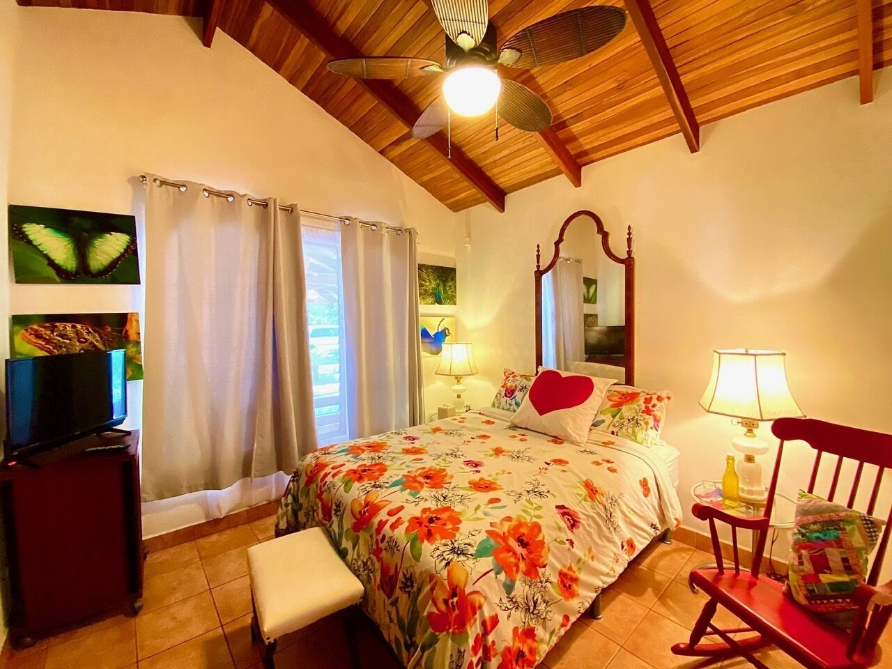 A bedroom with a bed, a chair, a TV, and a ceiling fan.